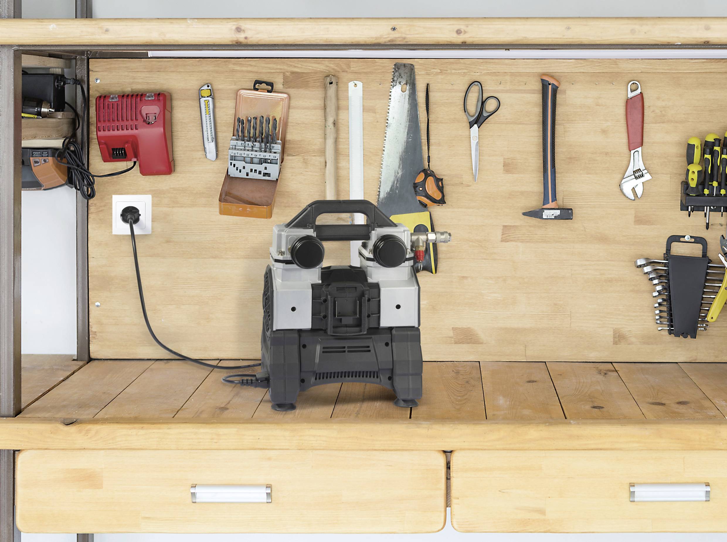 Werkbank mit verschiedenen Werkzeugen an der Rückwand: Feilen, Sägen, Scheren, Schraubenschlüssel. Eine elektrische Maschine steht mittig.