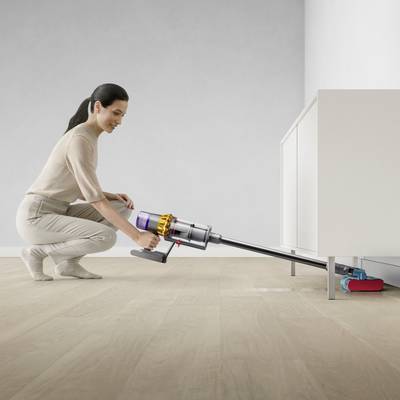 Eine Person saugt mit einem kabellosen Staubsauger unter einem niedrigen Schrank auf hellem Holzboden.