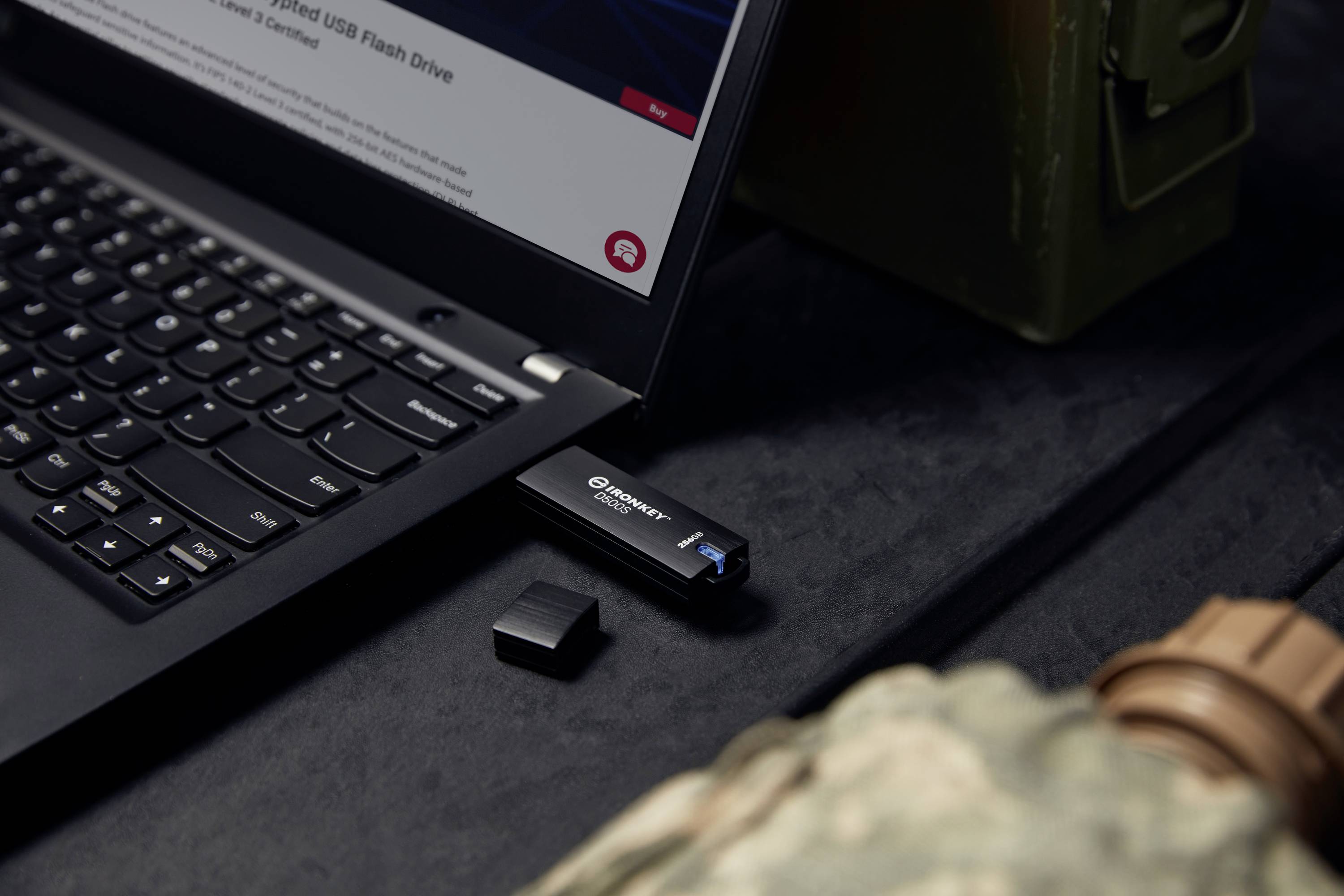 Ein USB-Stick ist an einem Laptop angeschlossen, neben einem geöffneten Deckel. Im Hintergrund befindet sich eine militärische Uniform.
