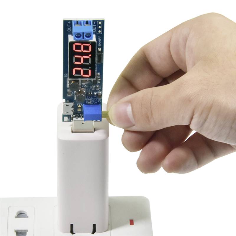 Eine Hand steckt einen USB-Stecker in ein Ladegerät mit einem digitalen Display, das '24.8' anzeigt.