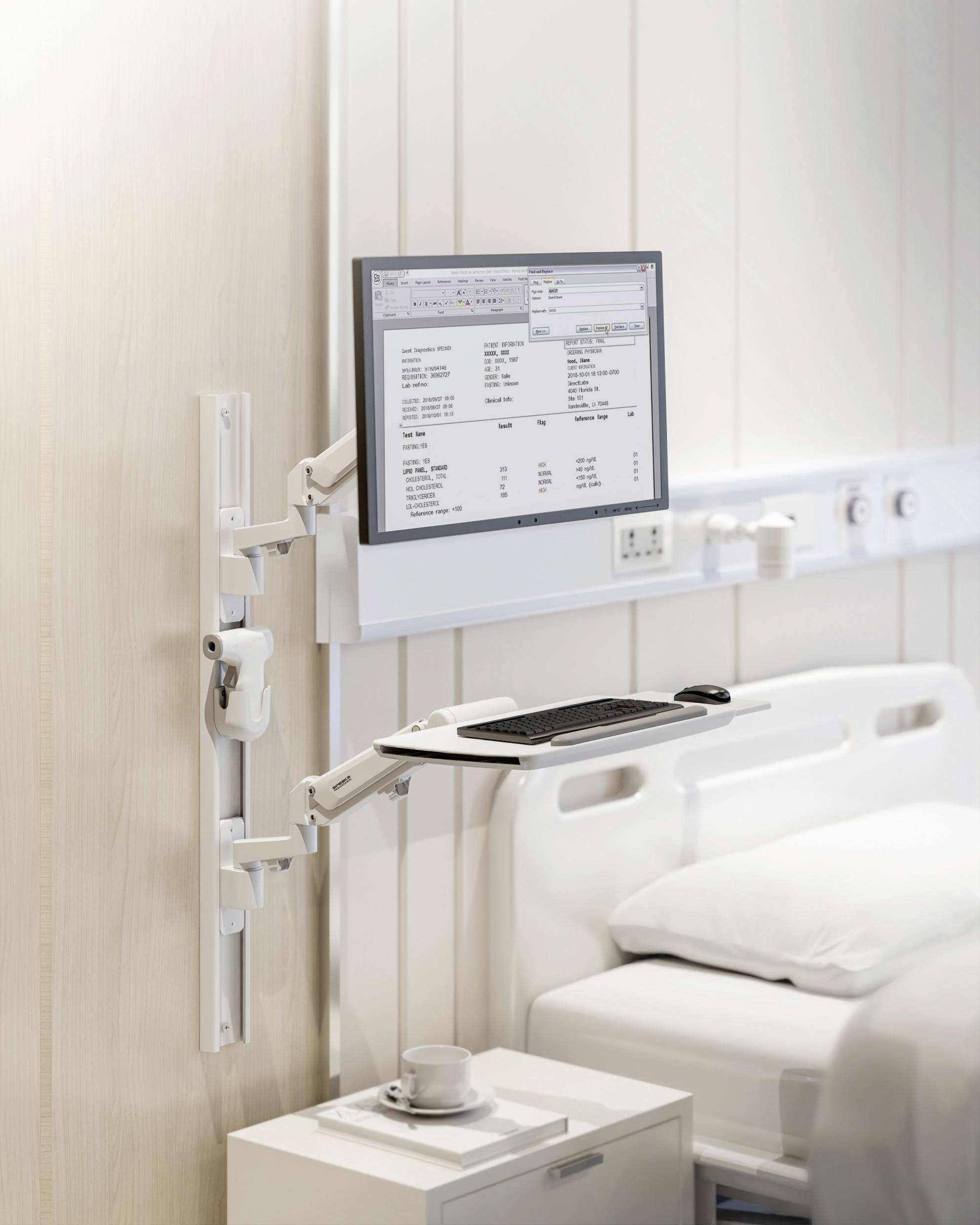 Ein Bildschirm mit medizinischen Informationen ist an der Wand neben einem Krankenhausbett montiert. Darunter befindet sich eine Tastatur.