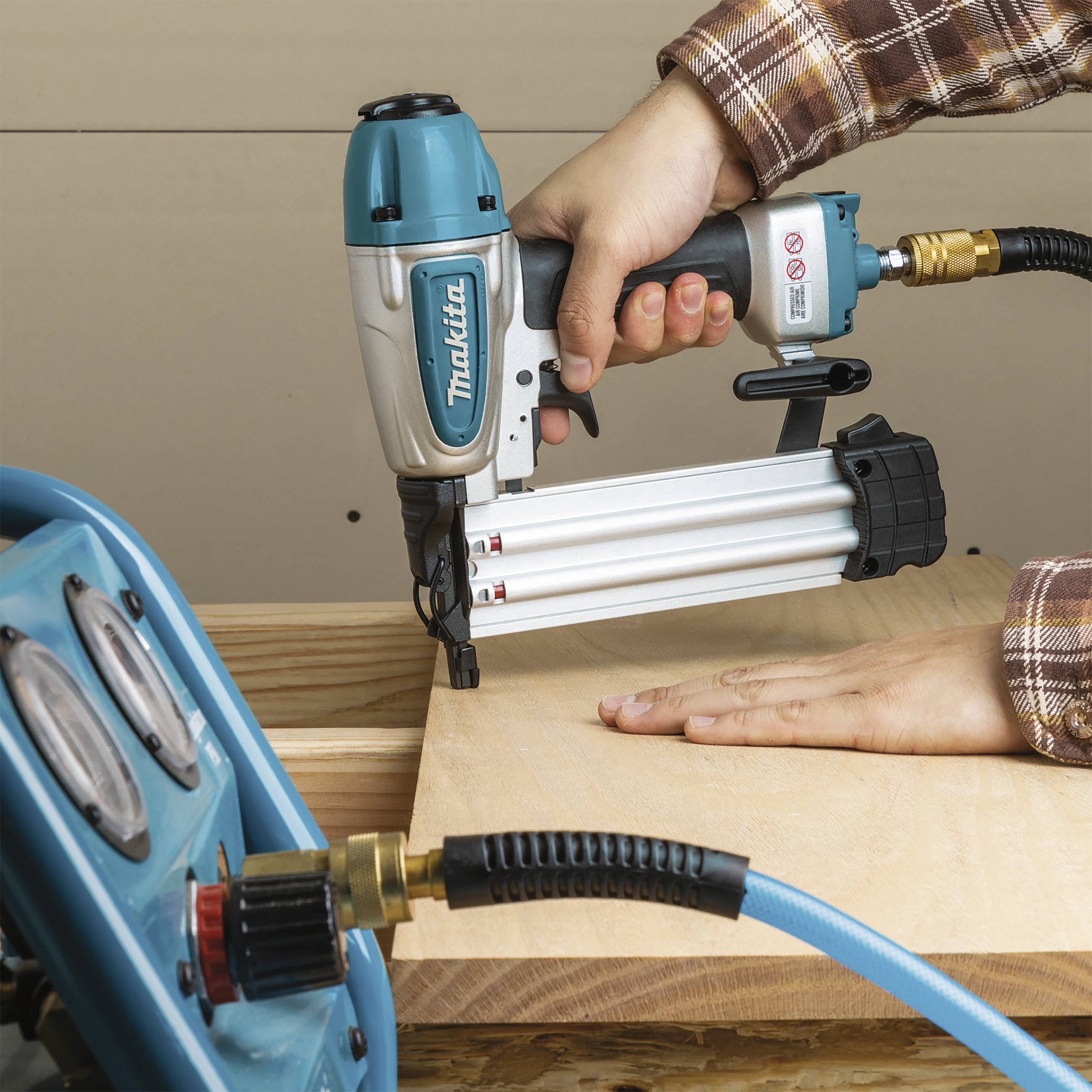 Eine Person arbeitet mit einem Druckluftnagler, um Holzplatten zu befestigen. Im Vordergrund ist ein Luftkompressor zu sehen.