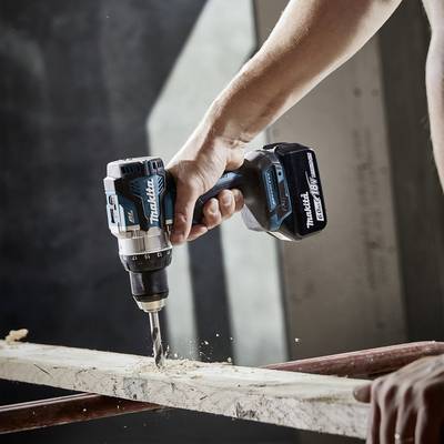 Eine Hand hält eine Bohrmaschine und bohrt ein Loch in ein Holzbrett. Holzspäne fliegen herum.