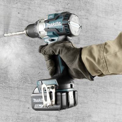 Ein Arbeiter bohrt mit einem kabellosen Makita-Bohrschrauber in eine Betonwand. Links drehen die Bohrmaschine und ein stabiler Bohrkopf.
