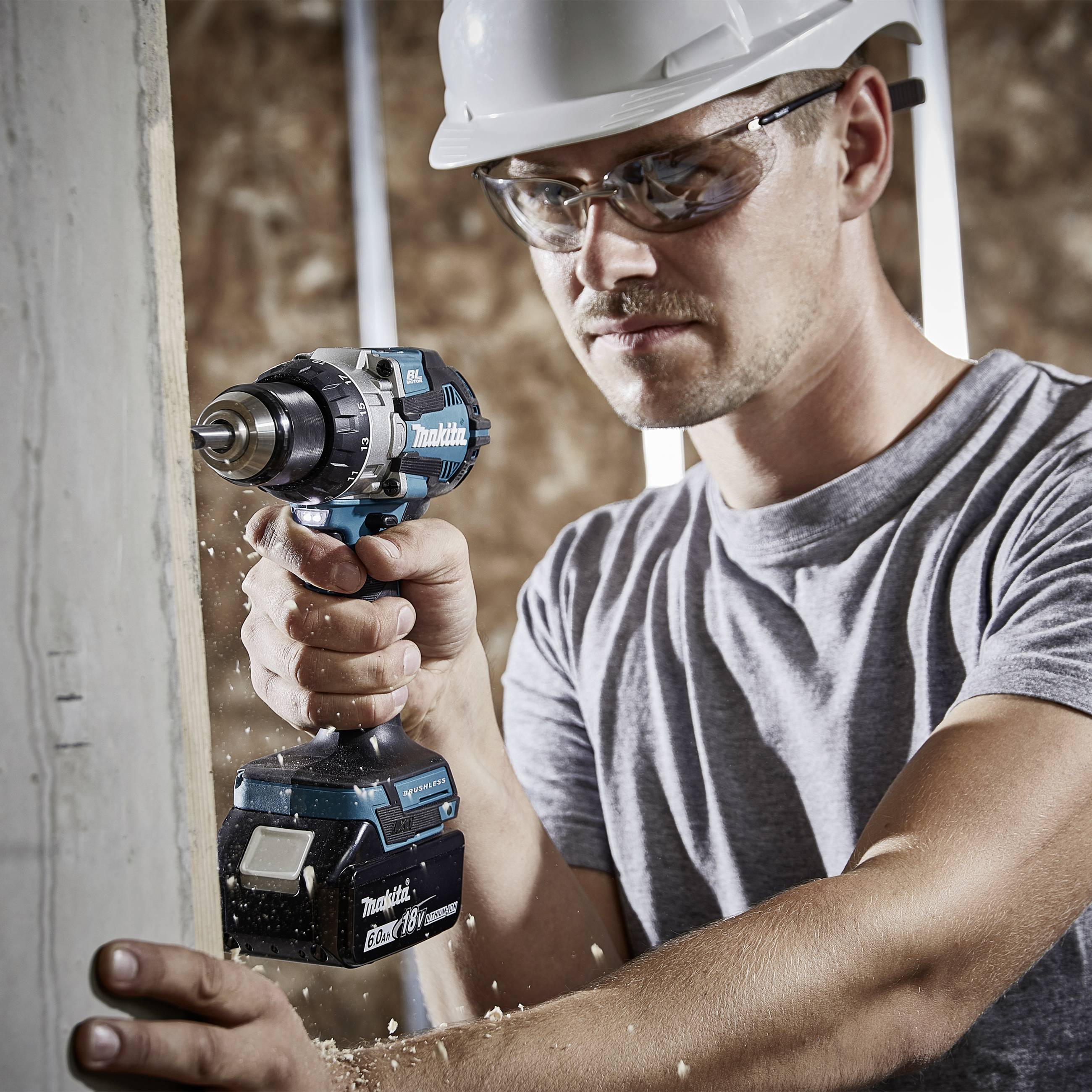 Ein Bauarbeiter mit Schutzhelm und Schutzbrille bohrt mit einem Akkuschrauber in eine Holzwand. Er konzentriert sich auf die Arbeit.