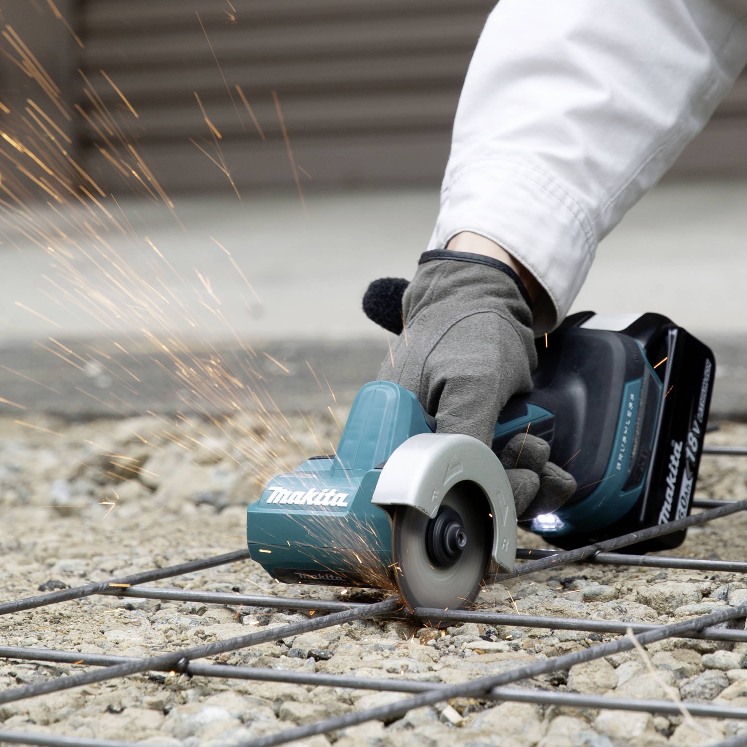 Eine Person schneidet mit einer kabellosen Schleifmaschine ein Metallgitter, Funken fliegen. Die Maschine ist türkisfarben.