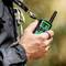 Person hält ein Walkie-Talkie mit Display, das die Zahl 8 anzeigt, in der Hand. Outdoor-Umgebung im Hintergrund.