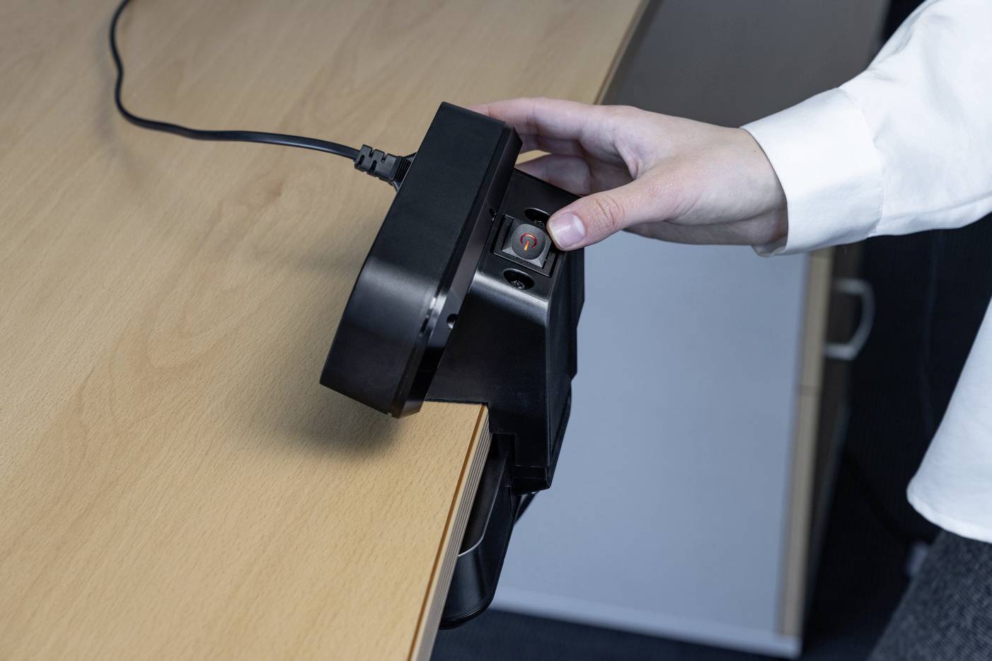 Eine Hand hält ein schwarzes Gerät, das an der Kante eines Holztisches befestigt wird.