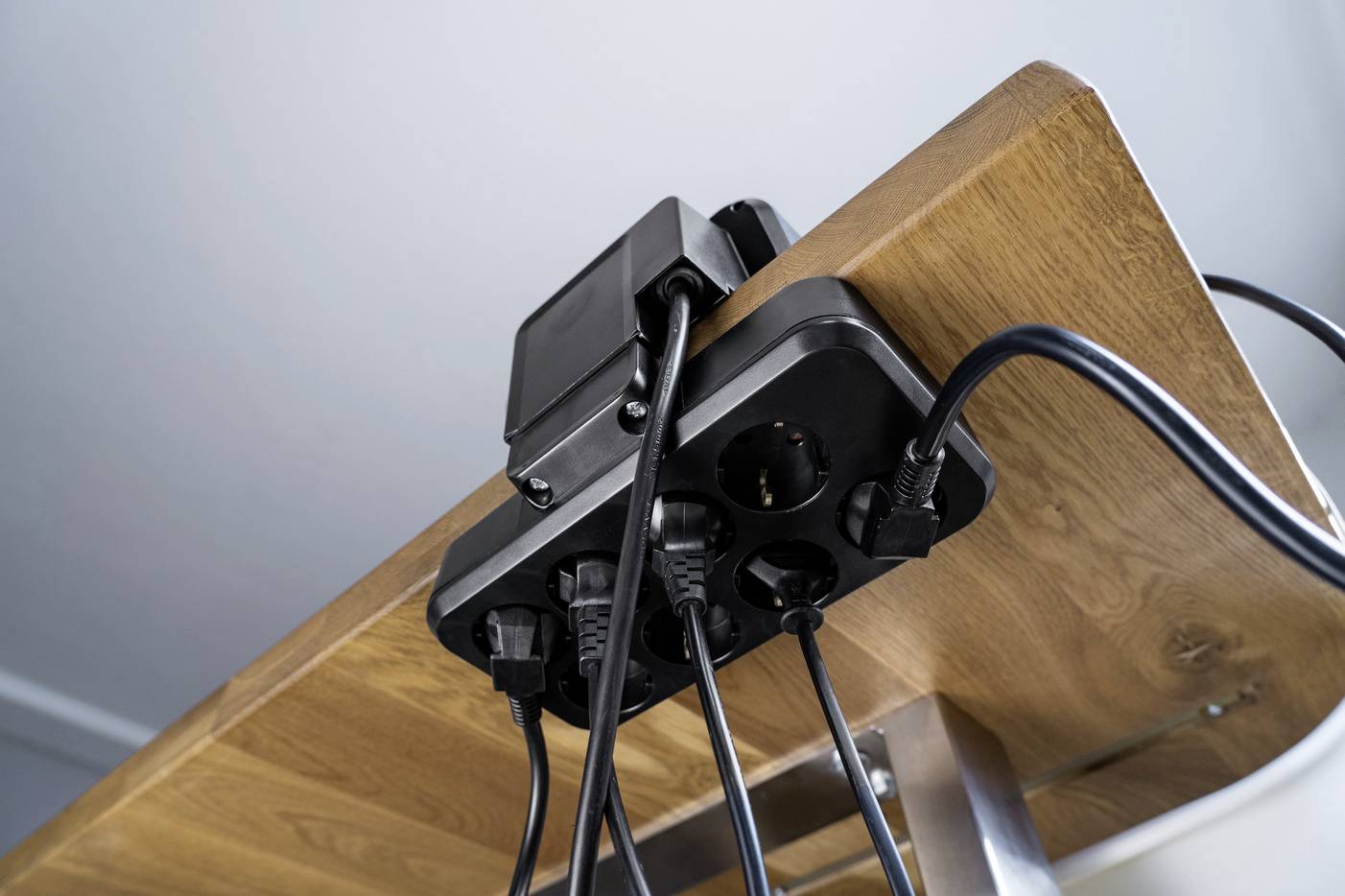 Mehrfachsteckdose unter einem Holztisch befestigt, verschiedene Kabel sind eingesteckt.