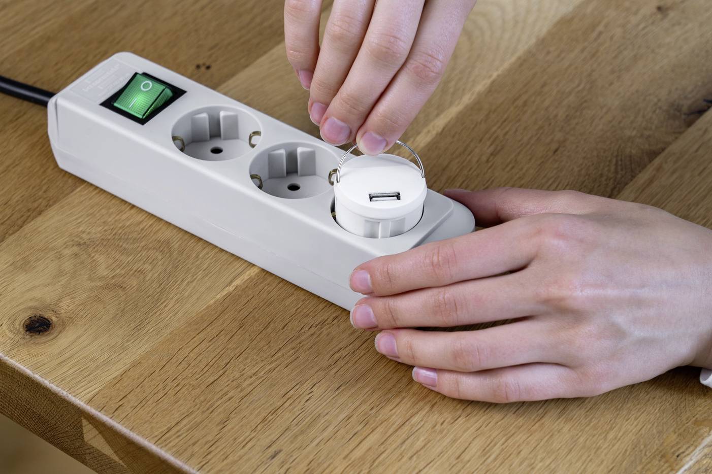 Eine Person setzt einen Kindersicherungsstecker in eine Steckdosenleiste ein, um die Steckdosen zu sichern.