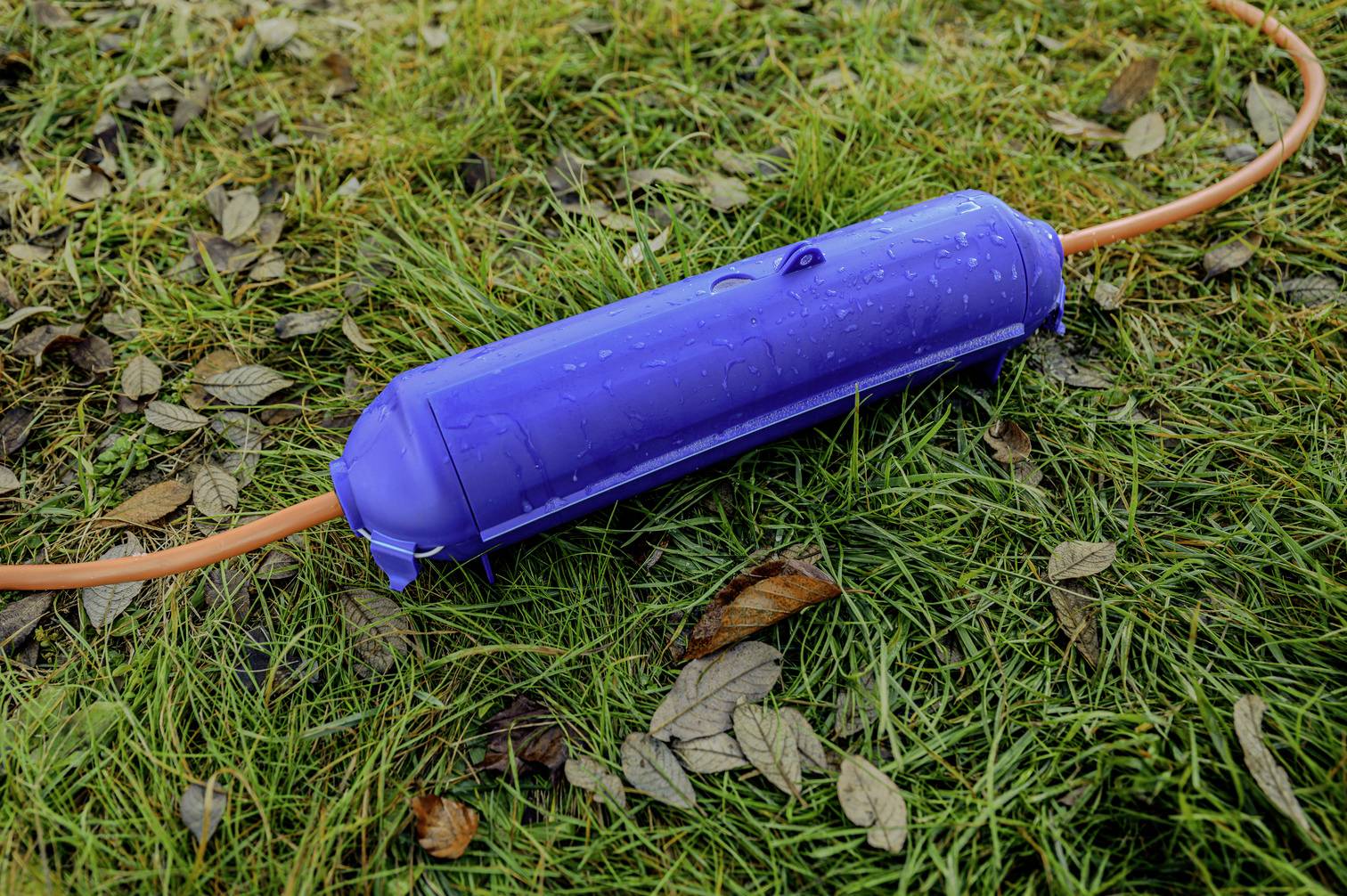 Ein blauer wasserdichter Kabelschutz liegt auf feuchtem Gras und Blättern, schützende Hülle für elektrische Kabel im Freien.