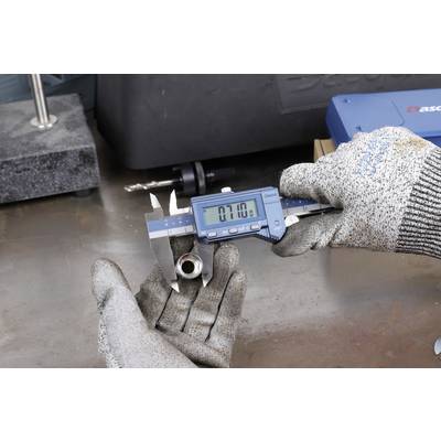 Person mit Handschuhen misst ein Metallteil mit einem digitalen Messschieber. Das Display zeigt '7.10'. Hintergrund hat Werkstattbedarf.