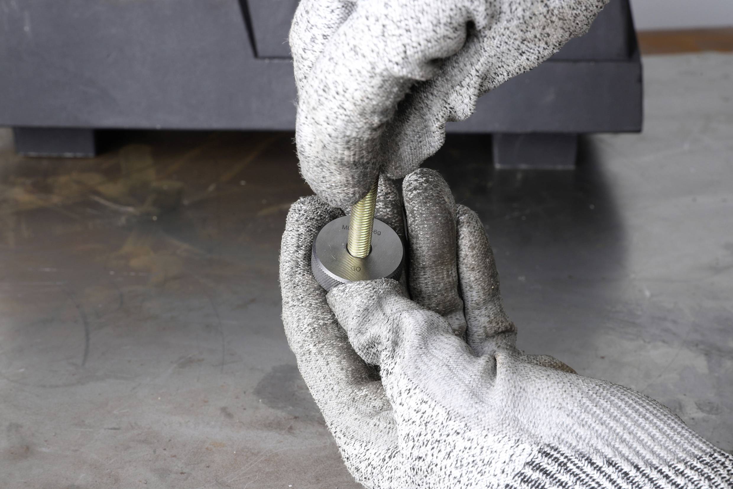 'Zwei behandschuhte Hände halten ein Metallteil mit einer Schraube in einer Werkstattumgebung.'