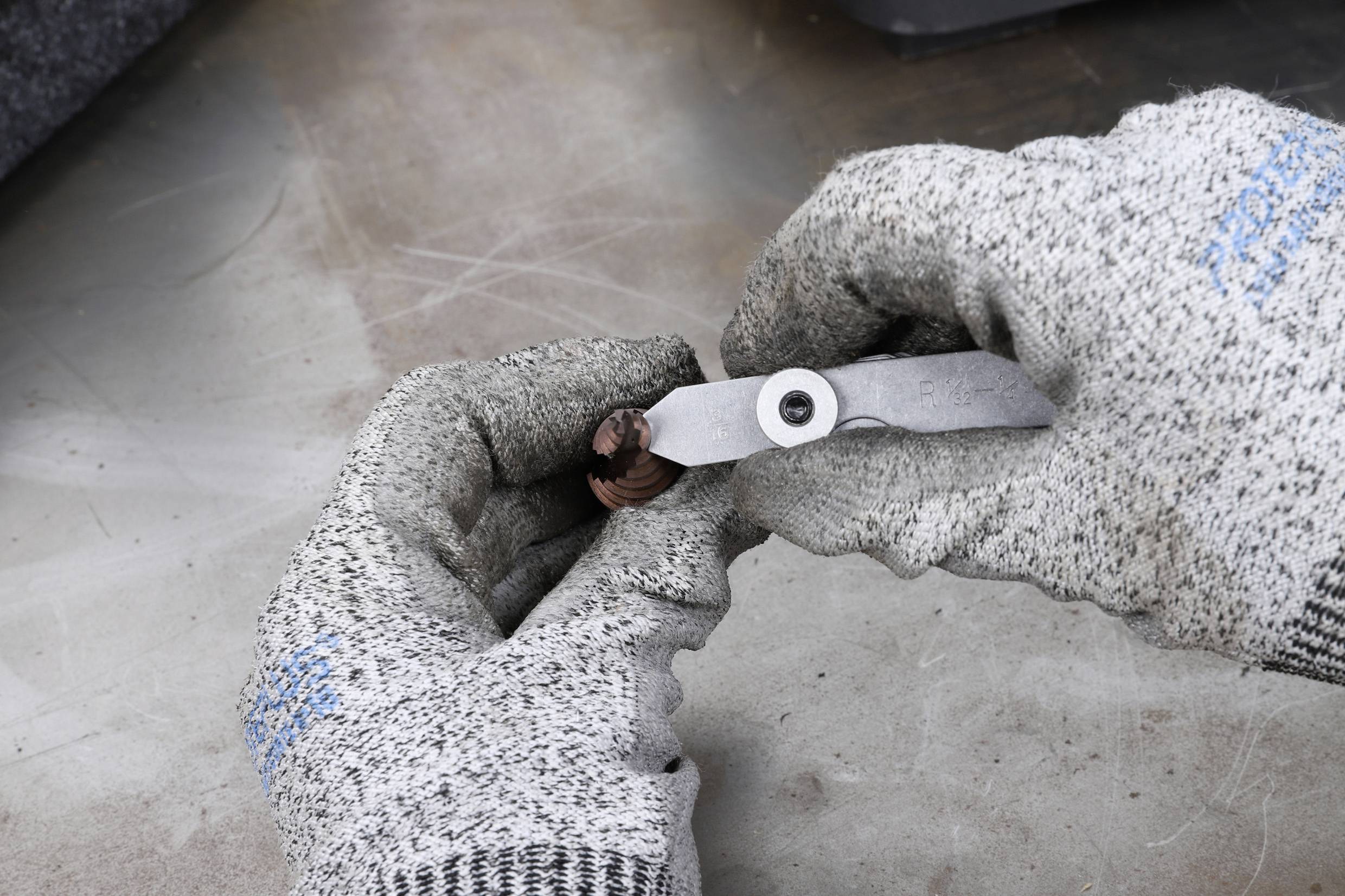 Eine Person trägt Arbeitshandschuhe und hält ein abgenutztes Metallteil mit einer Zange, wahrscheinlich bei einer Reparaturarbeit.