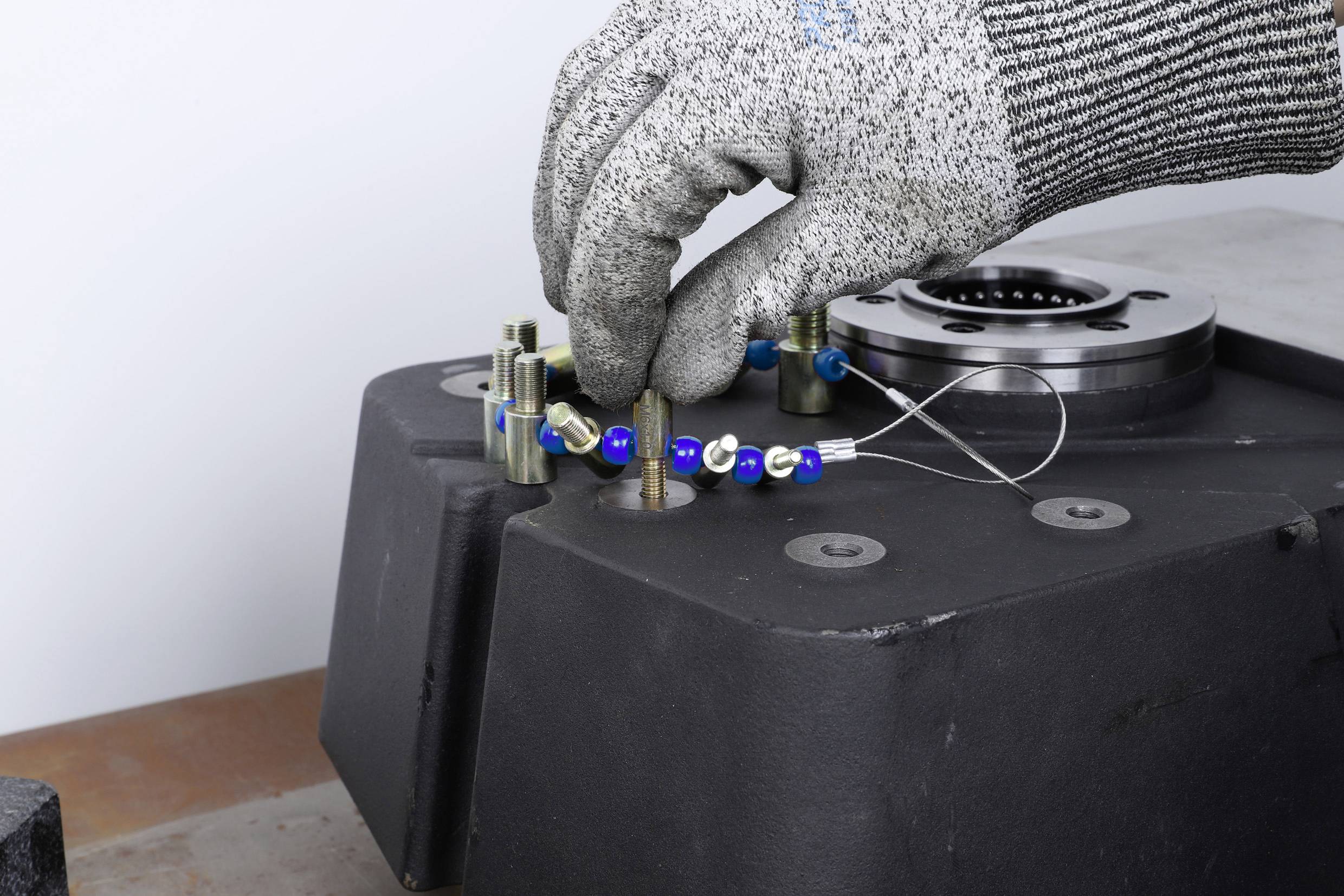 Eine Hand mit Handschuh montiert eine Kette aus blauen und silbernen Kugeln auf einen Metallstift, möglicherweise ein Arbeitsprozess.