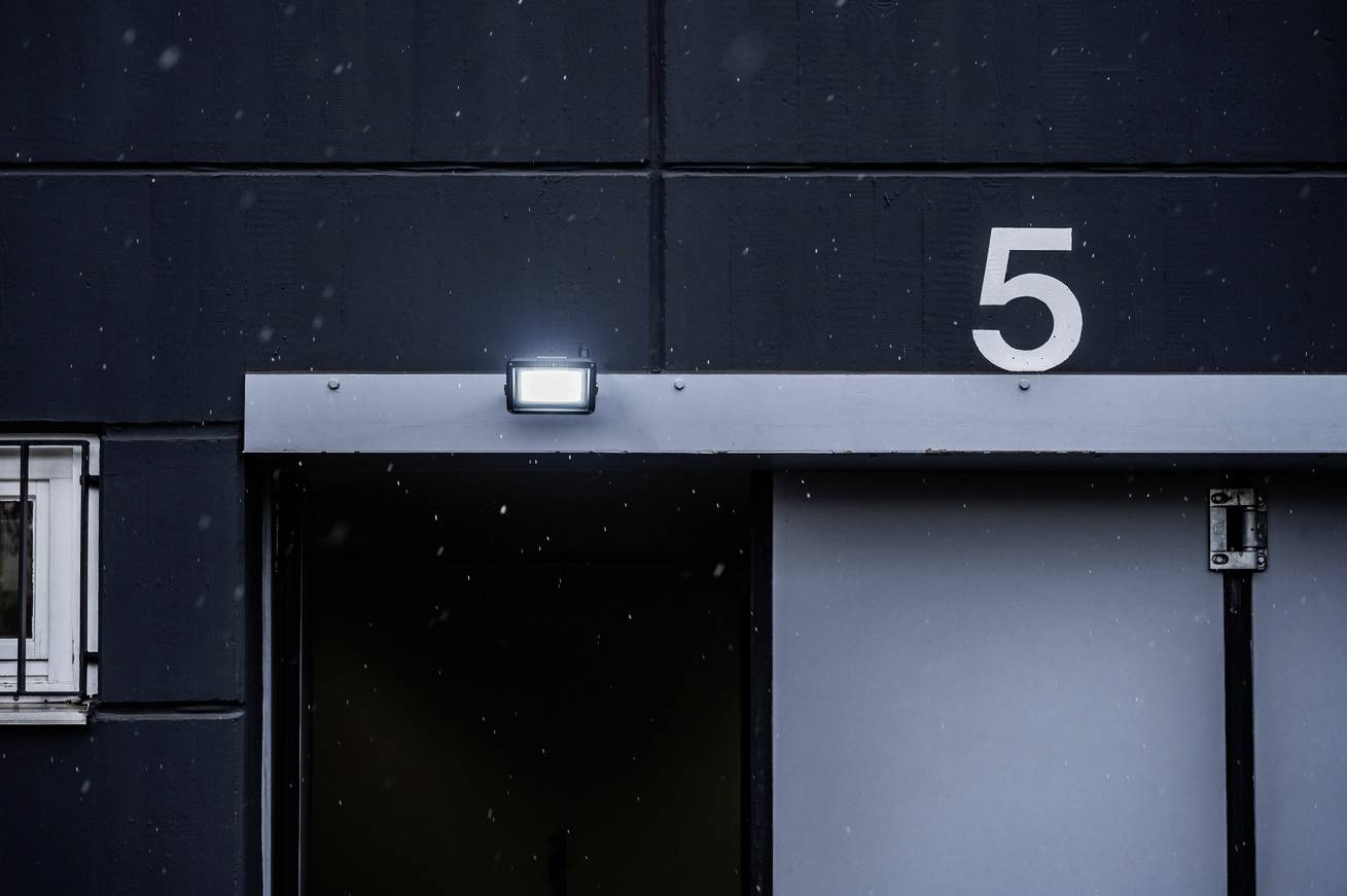 Geschlossene graue Tür eines Industriegebäudes mit der Zahl '5' darüber, beleuchtet von einer Lampe, leichte Schneeflocken fallen.