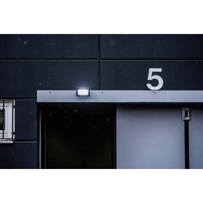 Geschlossene graue Tür eines Industriegebäudes mit der Zahl '5' darüber, beleuchtet von einer Lampe, leichte Schneeflocken fallen.