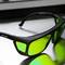 Eine schwarze Sonnenbrille mit grünen getönten Gläsern liegt auf einer glänzenden Metalloberfläche.