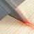 Nahaufnahme einer rotierenden Kreissäge, die ein Holzbrett durchtrennt. Ein roter Laserstrahl markiert die Schnittlinie.