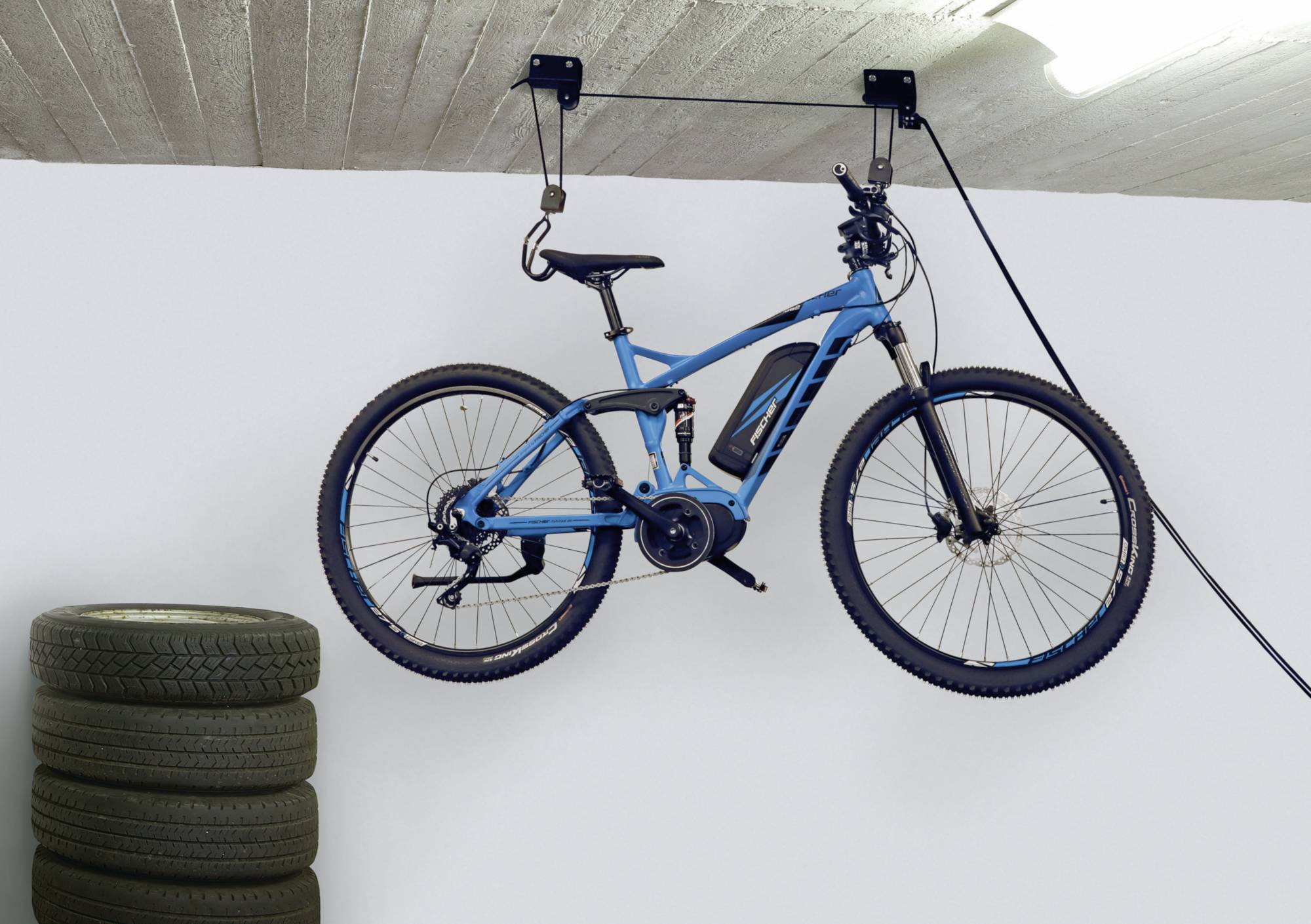 Blaues Fahrrad hängt an der Wand in einer Garage neben einem Stapel Reifen.