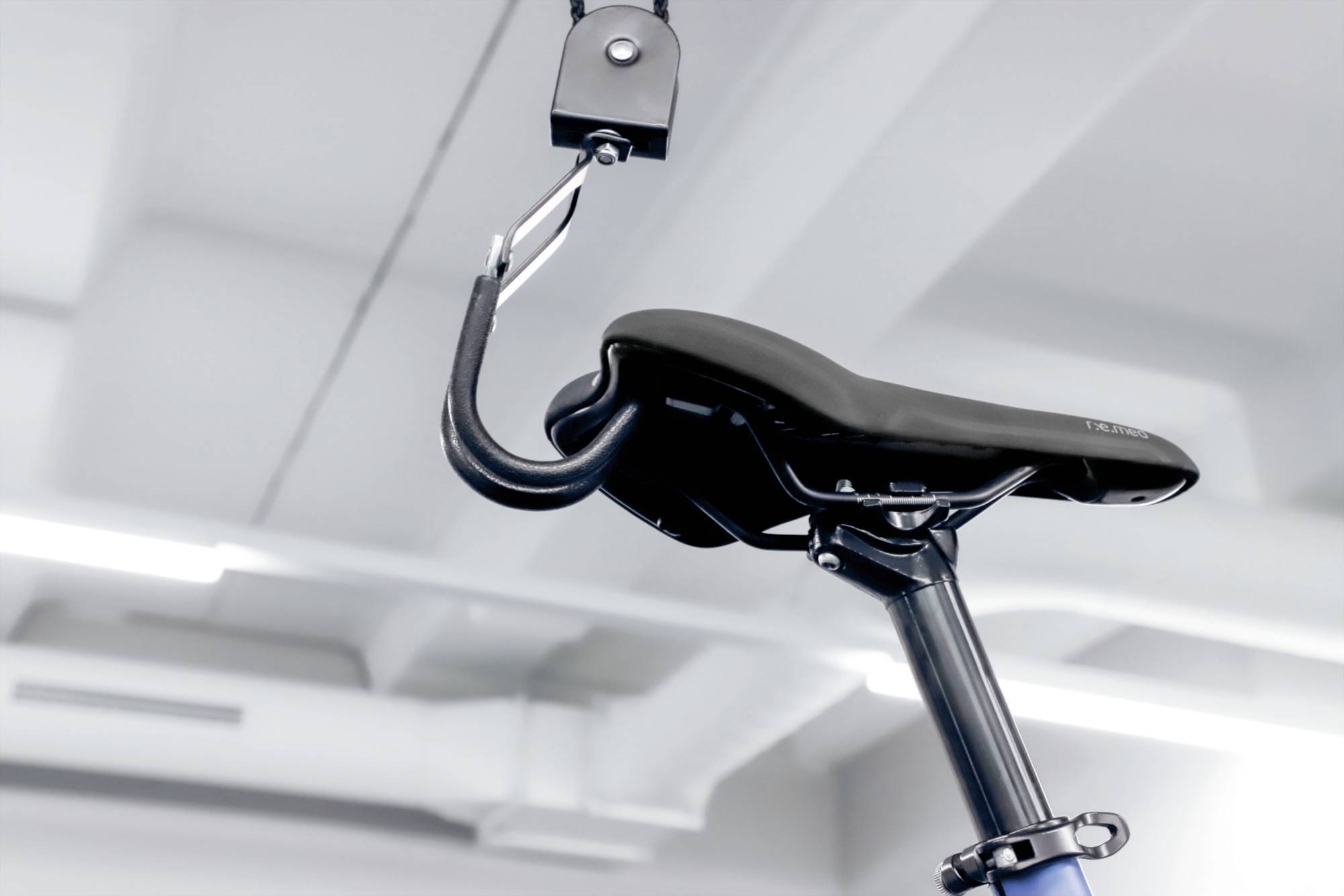 Ein Fahrradsattel hängt an einem Haken von der Decke in einem minimalistischen Raum.