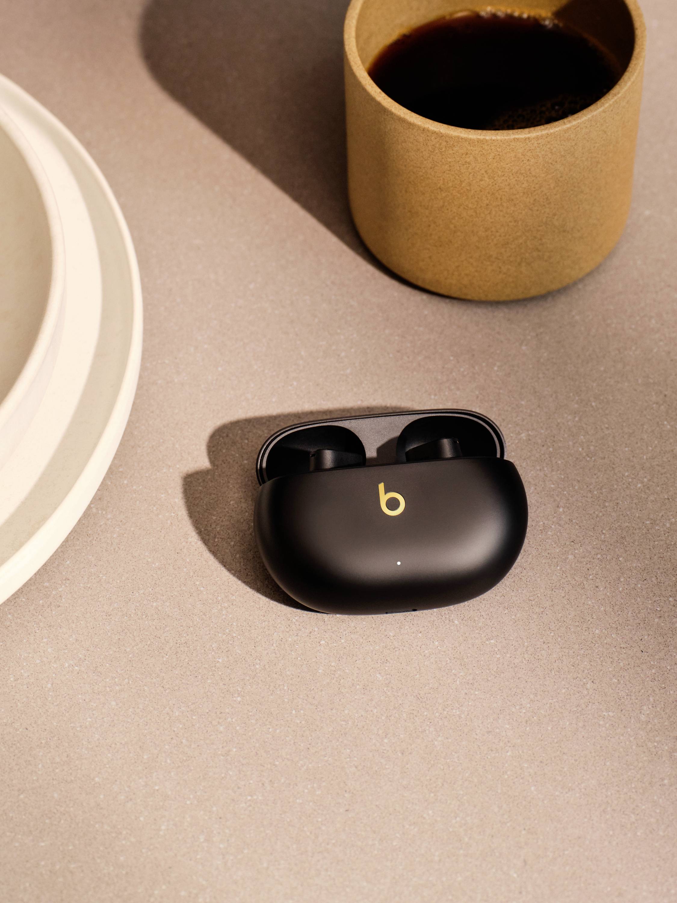 Kompakte, schwarze Kopfhörer in einer Ladehülle auf einem Tisch neben einer Tasse Kaffee.