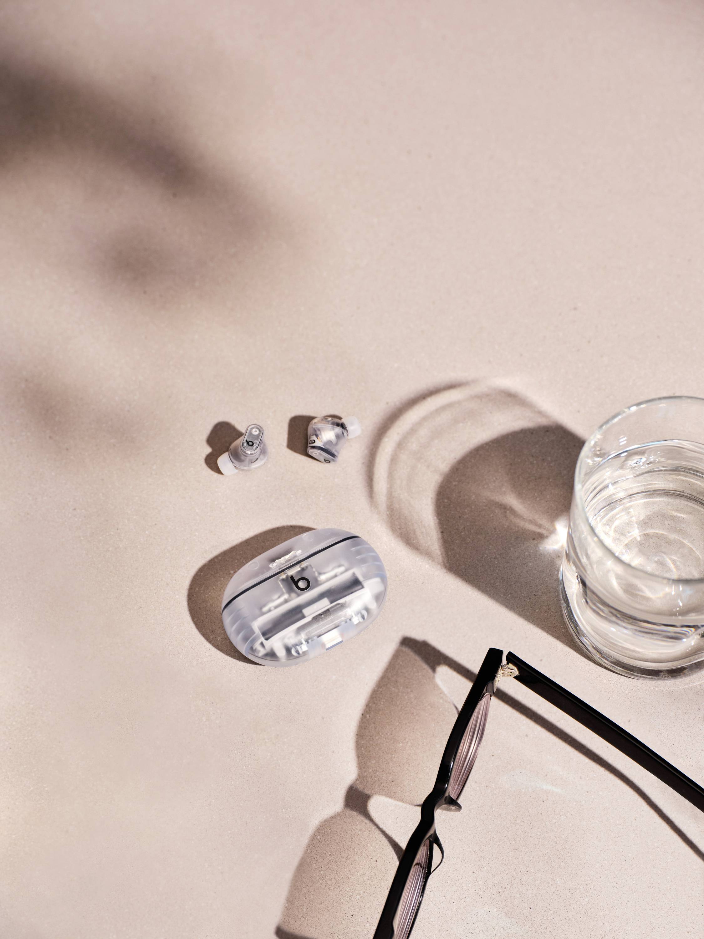 Ein Glas Wasser, eine Brille und kabellose Ohrhörer auf einem hellen Tisch.