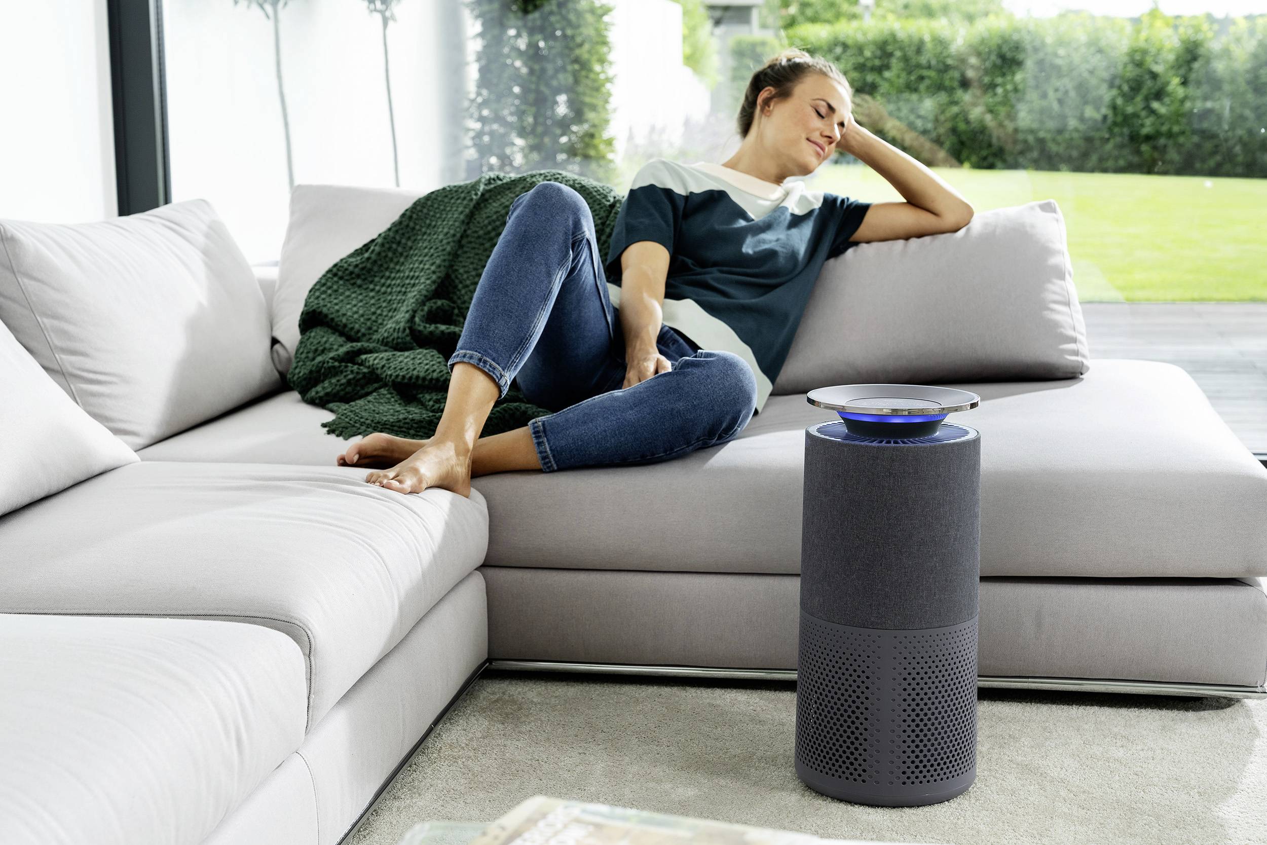 Eine Person entspannt sich auf einem Sofa in einem Wohnzimmer neben einem Smart-Lautsprecher.