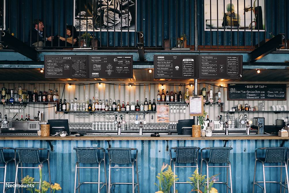 Blau dekorierte Bar mit drei Hockern, mehreren Zapfhähnen und Spirituosenflaschen. Oben sitzen Menschen an Tischen.