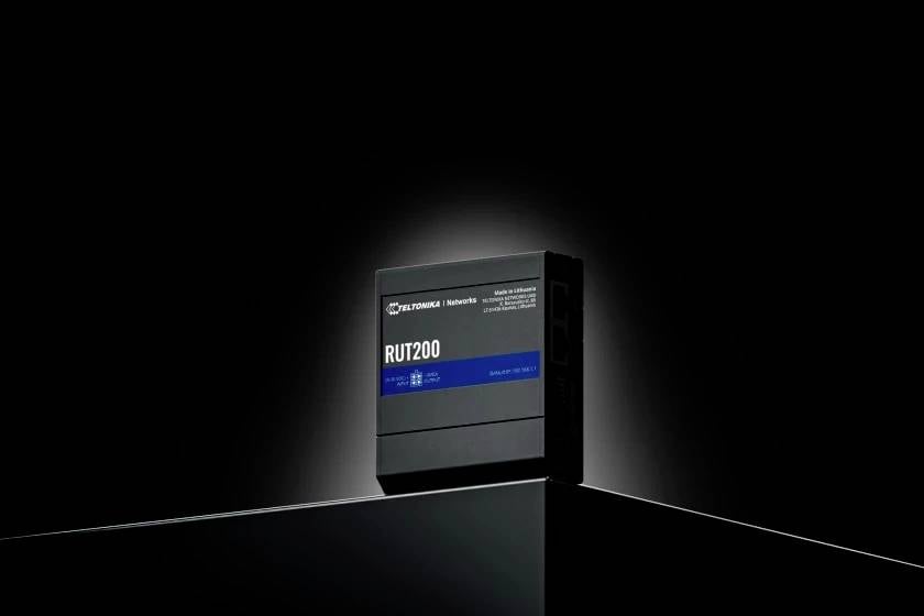 Ein schwarzer Router mit der Aufschrift 'RUT200', präsentiert auf einer reflektierenden Oberfläche und beleuchtet vor einem dunklen Hintergrund.