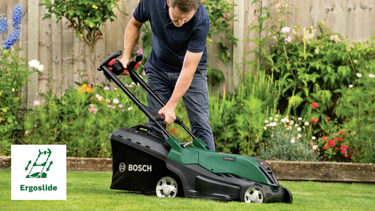 Mann mäht den Rasen mit einem Bosch Rasenmäher im Garten. Im Hintergrund blühen Blumen. Links unten das 'Ergoslide'-Logo.