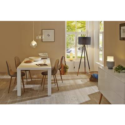 Ein Esszimmer mit einem weißen Tisch und vier Stühlen. Fenster lassen viel Licht herein. Auf dem Tisch liegen Zeitschriften und eine Schale Obst. Im Hintergrund steht eine Stehlampe.