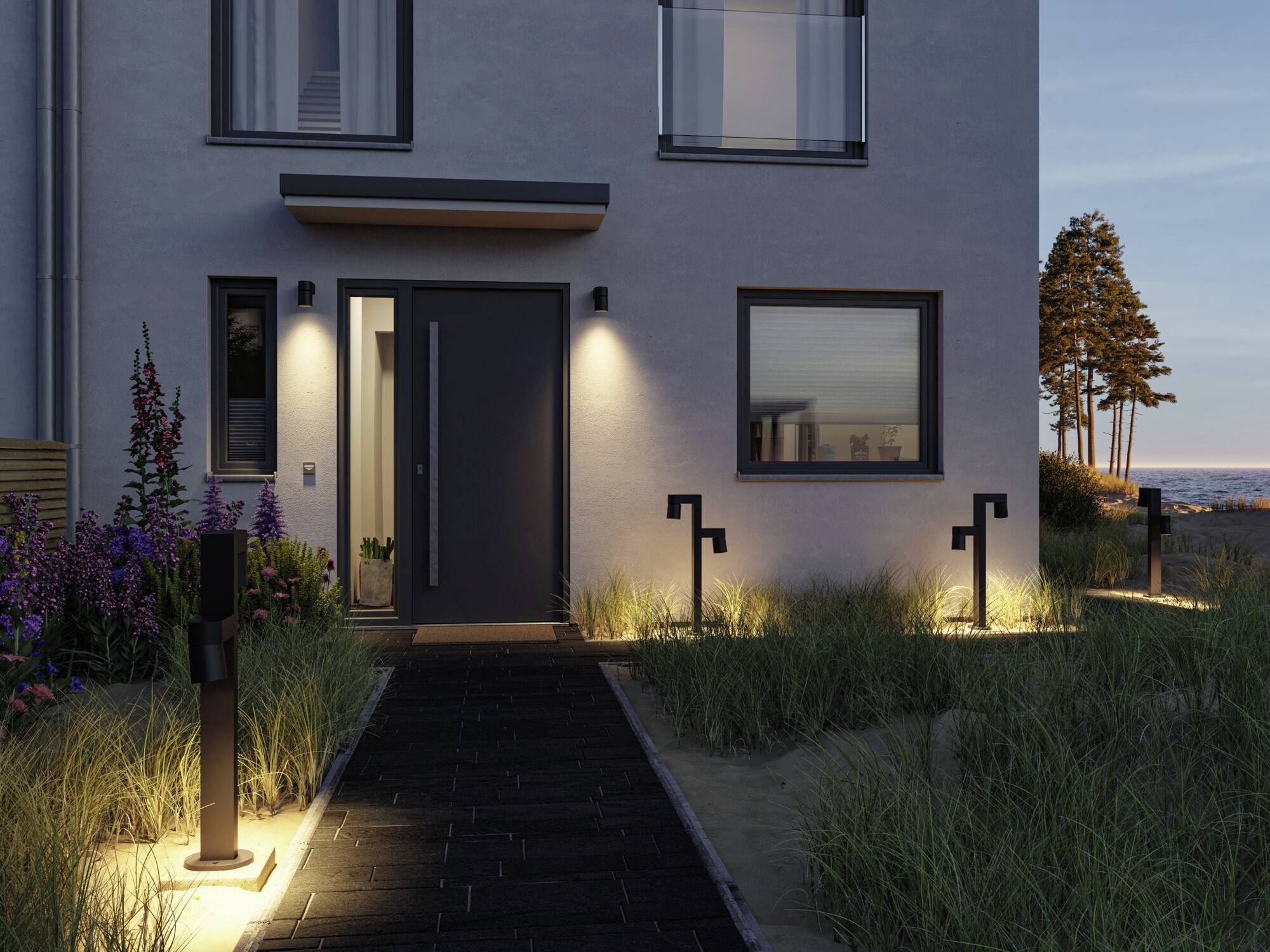Beleuchteter Pfad zu einem modernen Haus bei Dämmerung, umgeben von Gräsern und Gartenlampen. Im Hintergrund stehen Bäume.