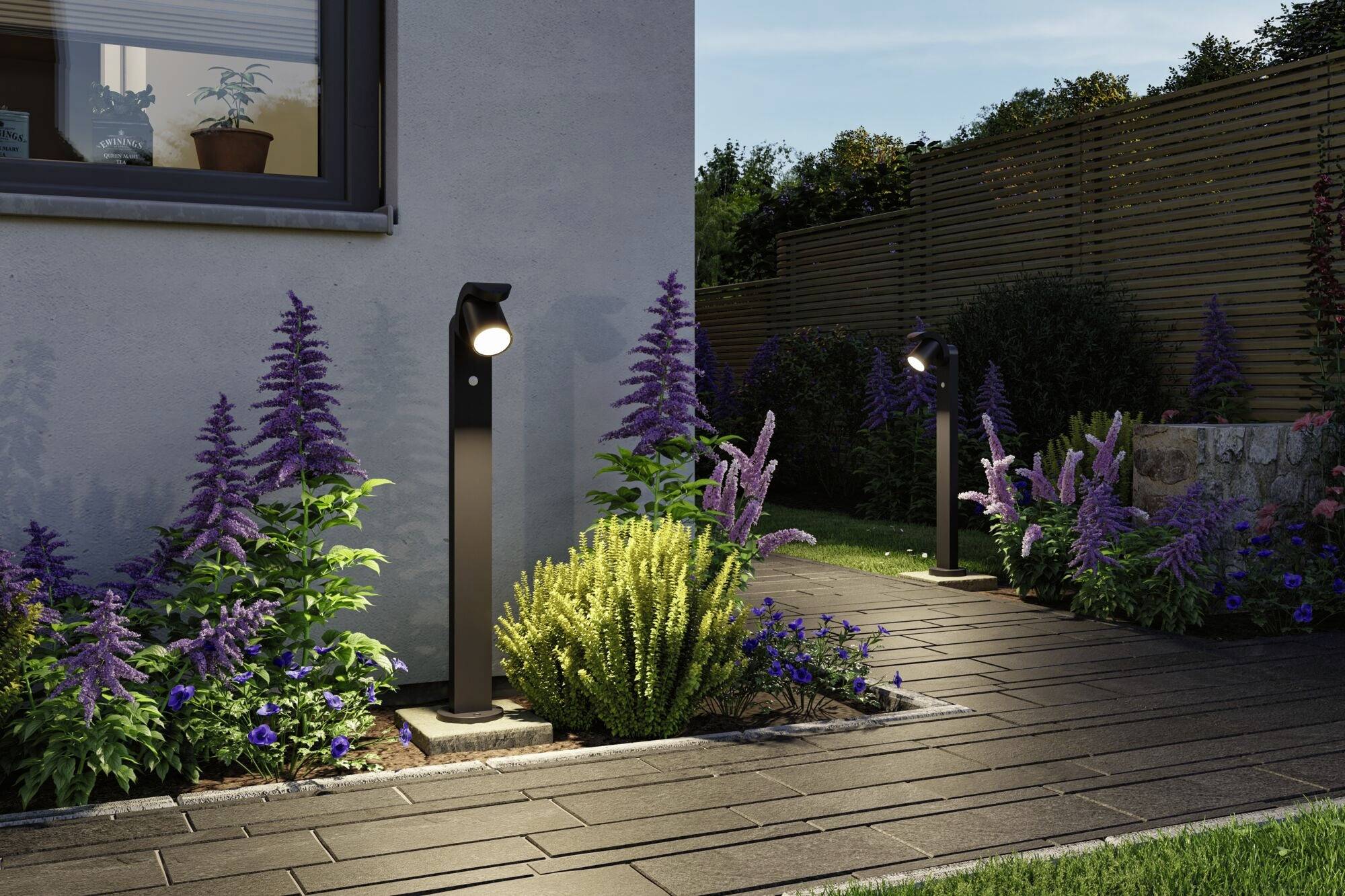 Ein stilvoll beleuchteter Gartenweg mit blühenden lila Blumen und grünen Sträuchern an einem Haus, Dämmerungshimmel im Hintergrund.