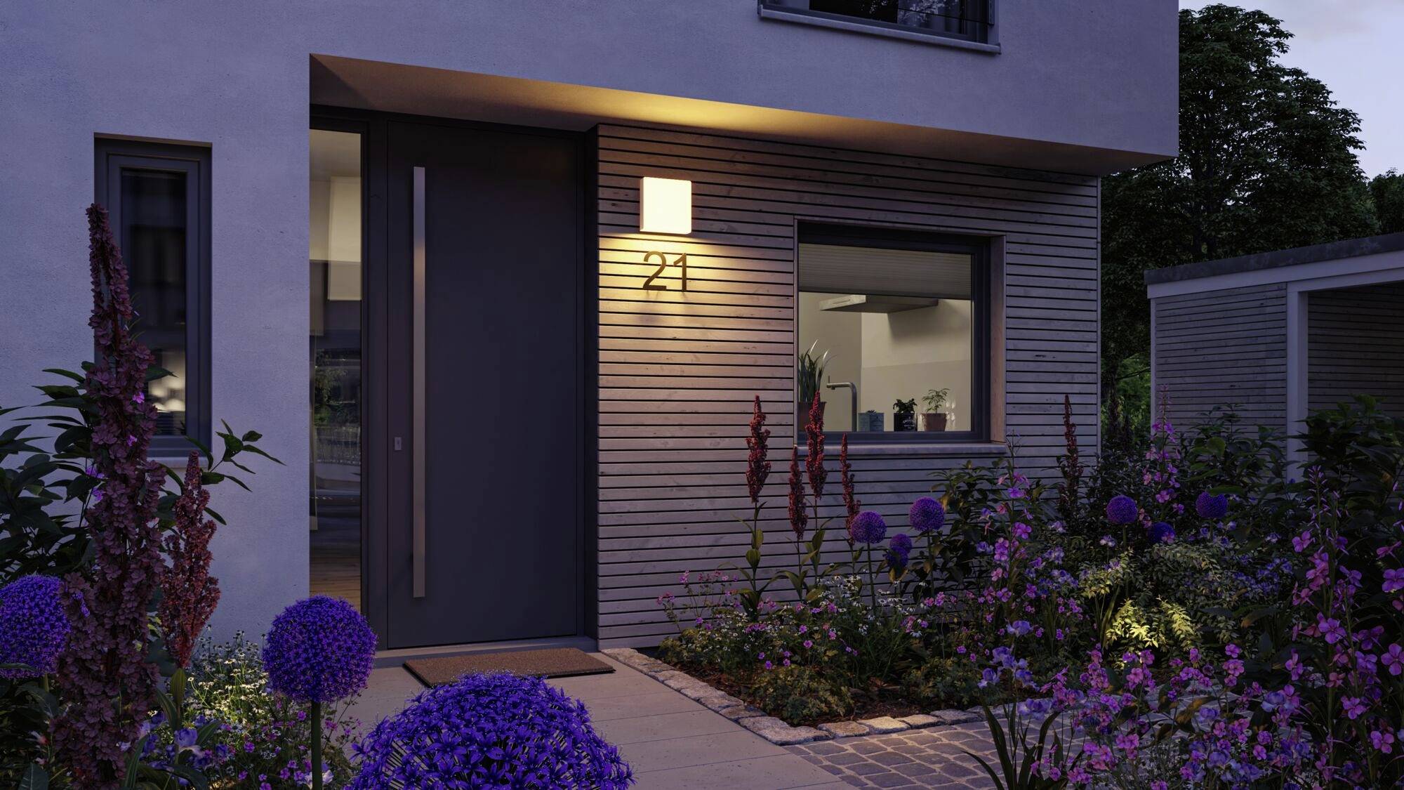 Moderne Hausfassade bei Dämmerung mit Glasfenster und Tür. Beleuchtet von Außenleuchte neben der Hausnummer 21. 