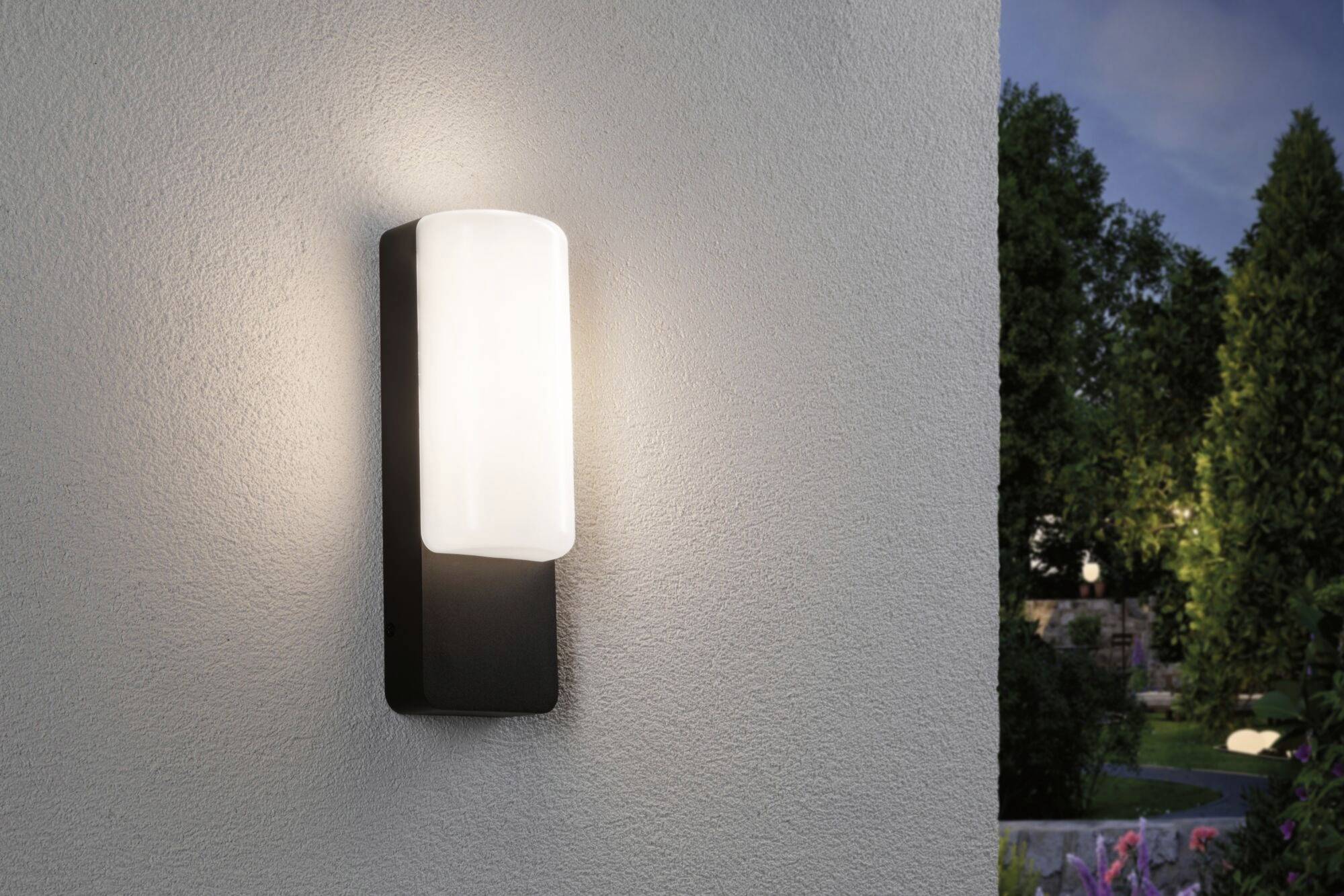 Wandleuchte mit modernem Design beleuchtet eine Außenwand in einer abendlichen Gartenumgebung.