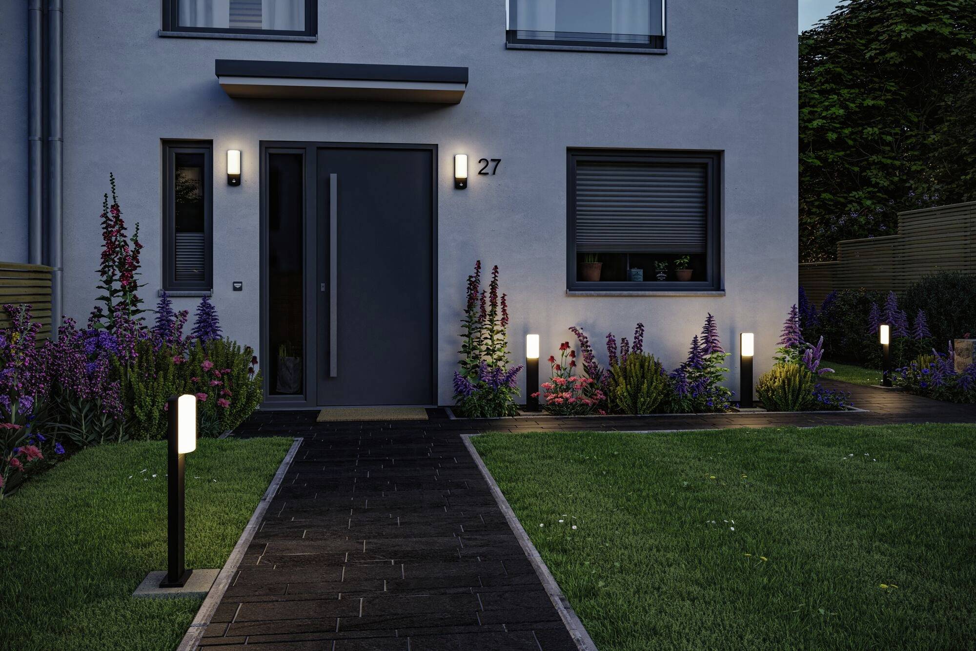 Eingang eines modernen Hauses in der Dämmerung, umgeben von beleuchteten Gartenwegen und blühenden Pflanzen.
