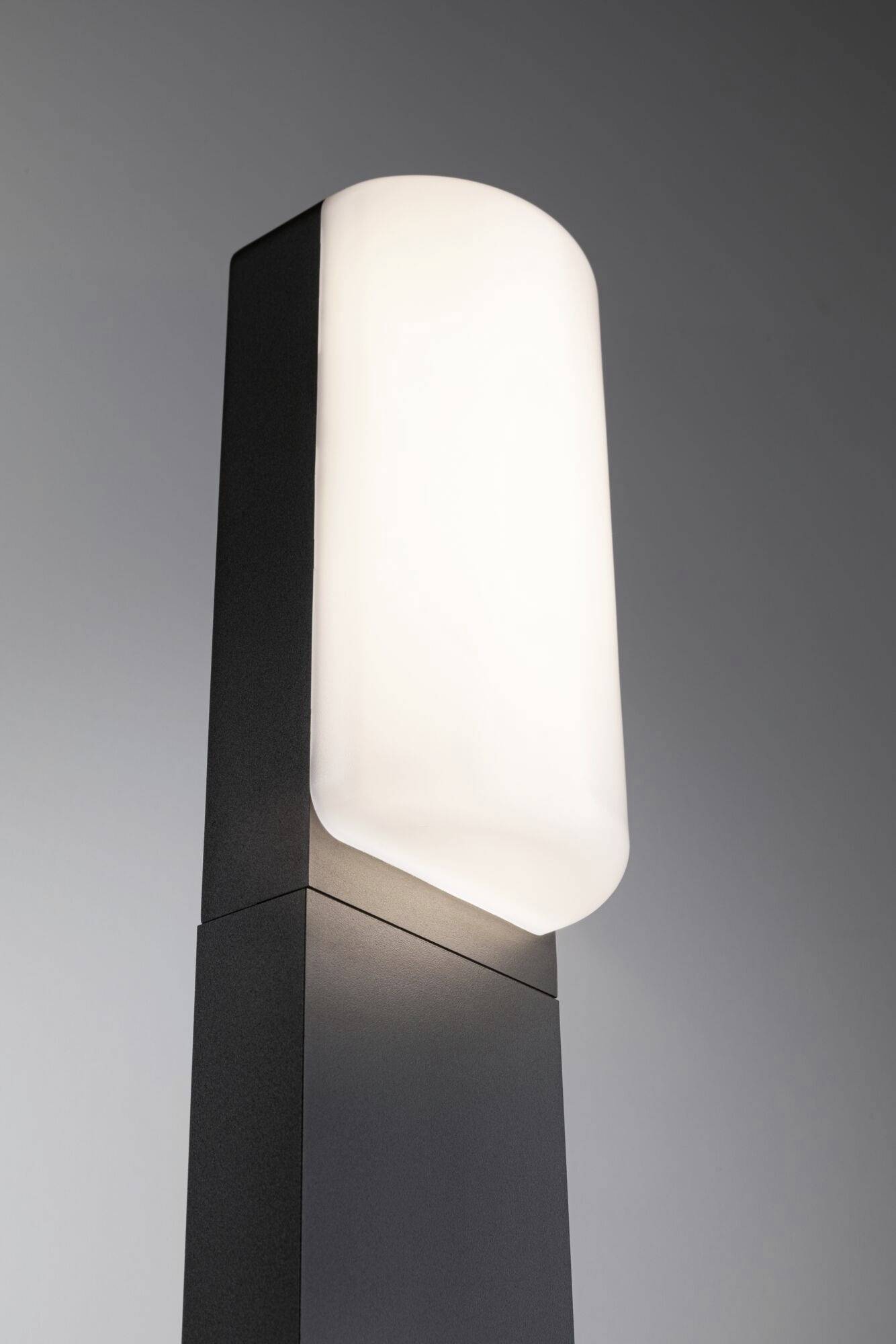 Eine moderne Stehlampe mit rechteckigem, schwarzem Sockel und abgerundetem, beleuchtetem Schirm vor grauem Hintergrund.