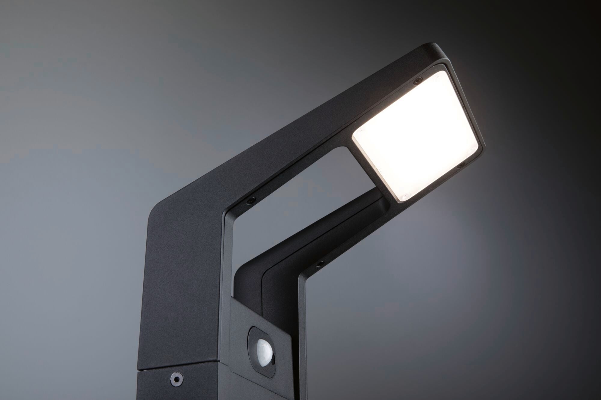 Eine moderne schwarze LED-Lampe mit quadratischem Leuchtkopf, der nach unten strahlt, in einem dunklen Hintergrund fotografiert.