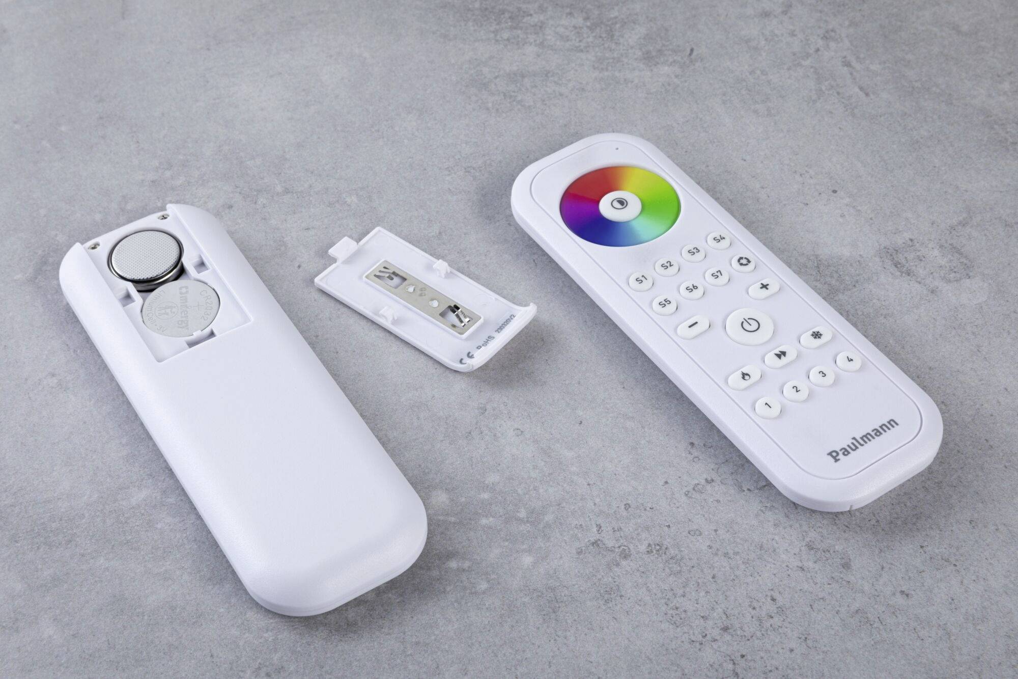 Weiße Fernbedienung mit abnehmbarer Rückseite, Batteriefach sichtbar. Vorderseite mit Farbkreis und Tasten für Lichtsteuerung.