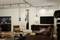 Wohnzimmer mit braunen Sofas, modernen Hängeleuchten, großem Wandbild und Flachbildfernseher, Holzboden und Küche im Hintergrund.