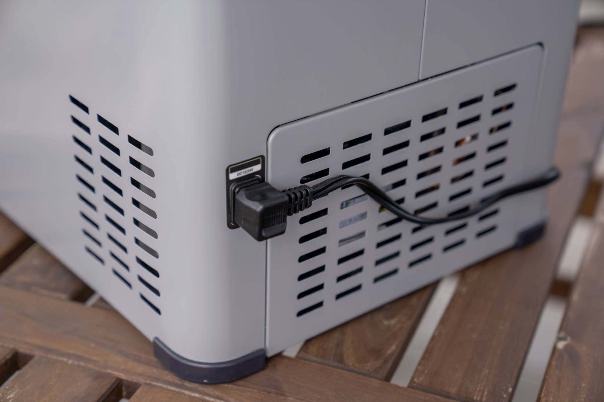 Ein grauer Luftreiniger steht auf einem Holztisch. Ein Stromkabel ist an der Rückseite des Geräts angeschlossen.