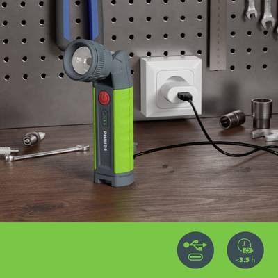 Das Bild zeigt eine grüne Taschenlampe, angeschlossen an eine Steckdose, auf einer Holzoberfläche vor einer perforierten Wand mit Werkzeugen.