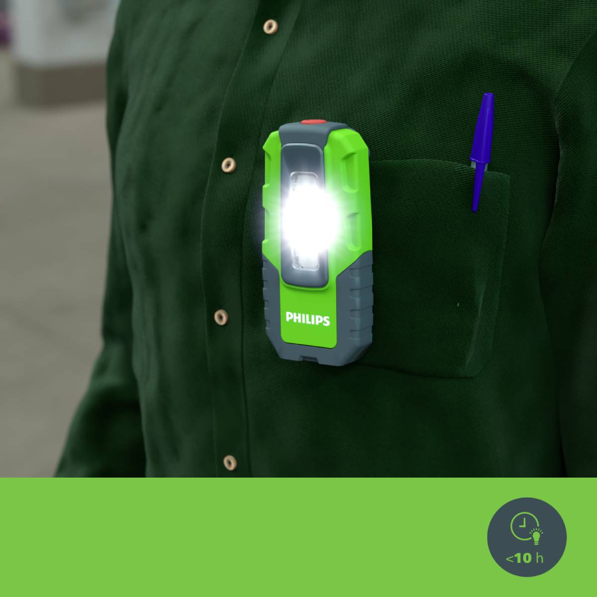 Eine grüne Arbeitsjacke mit einer leuchtenden, handlichen Lampe in der Brusttasche, daneben ein blauer Kugelschreiber.