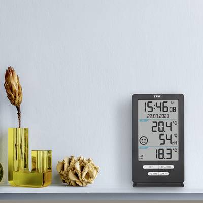 Ein digitales Thermometer zeigt die Temperatur 20,4°C und Luftfeuchtigkeit 54% an. Daneben steht eine gelbe Vase mit einer getrockneten Blume.