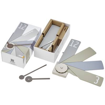 Verpackung einer Designeruhr aus Karton mit aufgeklapptem Rad und lackierten Platten in verschiedenen Grautönen, neben Zubehörteilen.