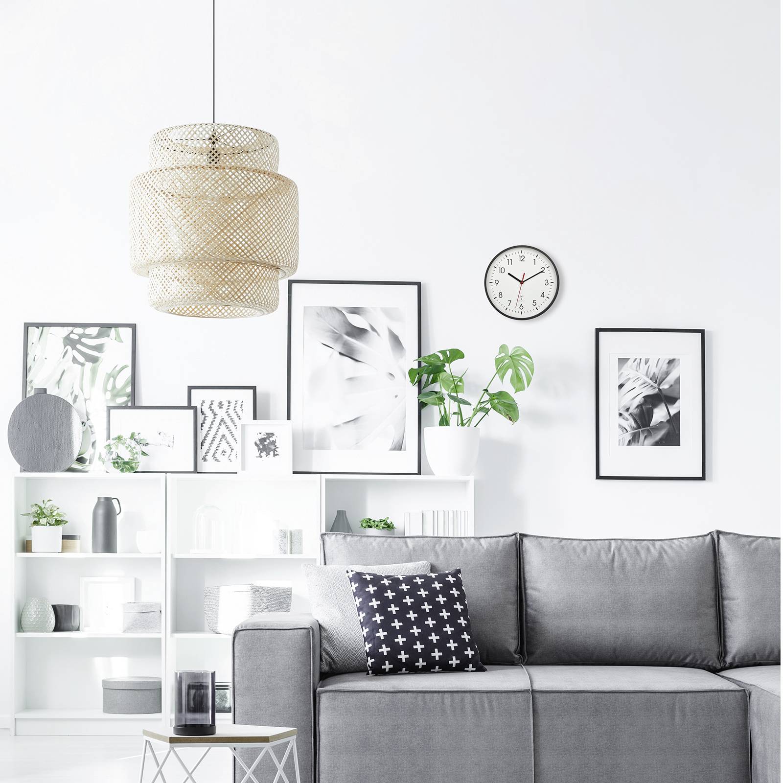 Helles Wohnzimmer mit grauem Sofa, schwarzen Kissen und Pflanze; moderne Kunst an weißen Wänden, runde Uhr zeigt 9:25 an.