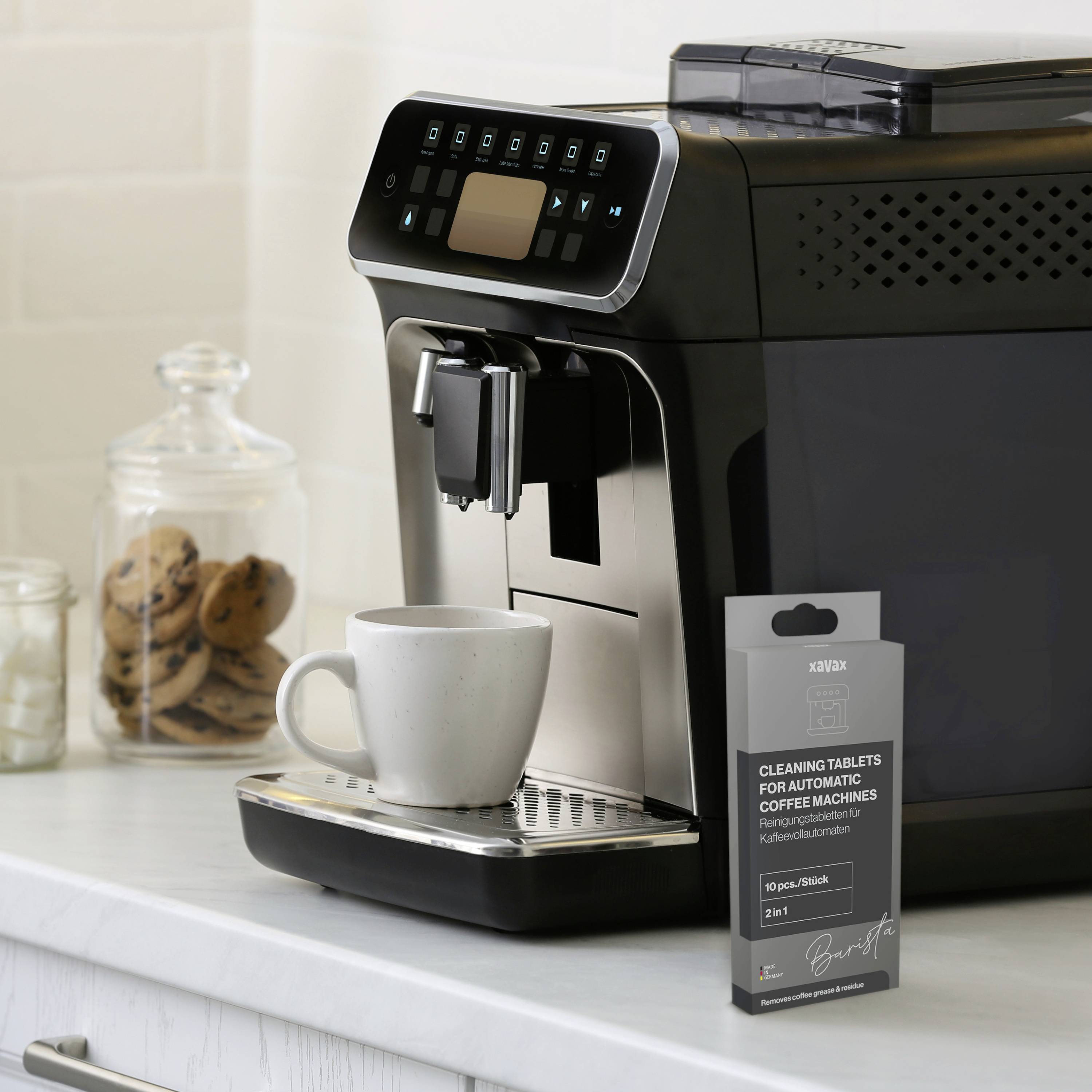 Schwarze Kaffeemaschine mit Display steht auf Küchenarbeitsplatte. Daneben eine Packung Reinigungstabletten und ein weißer Becher. Im Hintergrund Keksglas und Milch.