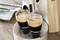 Zwei Espresso in Gläsern werden gleichzeitig aus einer Kaffeemaschine gegossen. Die Maschine steht auf einer Holzoberfläche.