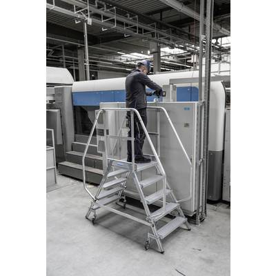 Ein Techniker arbeitet auf einer Metallplattform vor einem großen, industriellen Drucker in einer Fabrikumgebung.